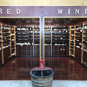 Wine rack with shelves stocked with bottles, a barrel, and 'Red Wine' sign.