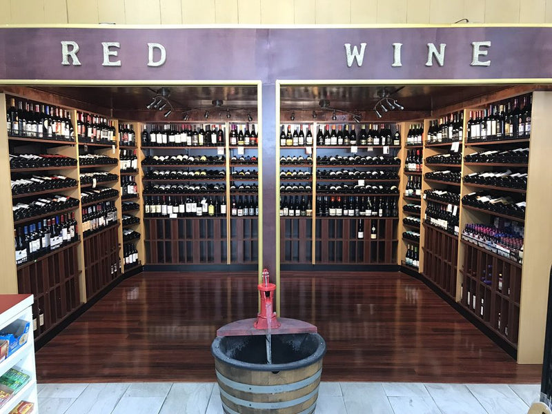 Wine rack with shelves stocked with bottles, a barrel, and 'Red Wine' sign.